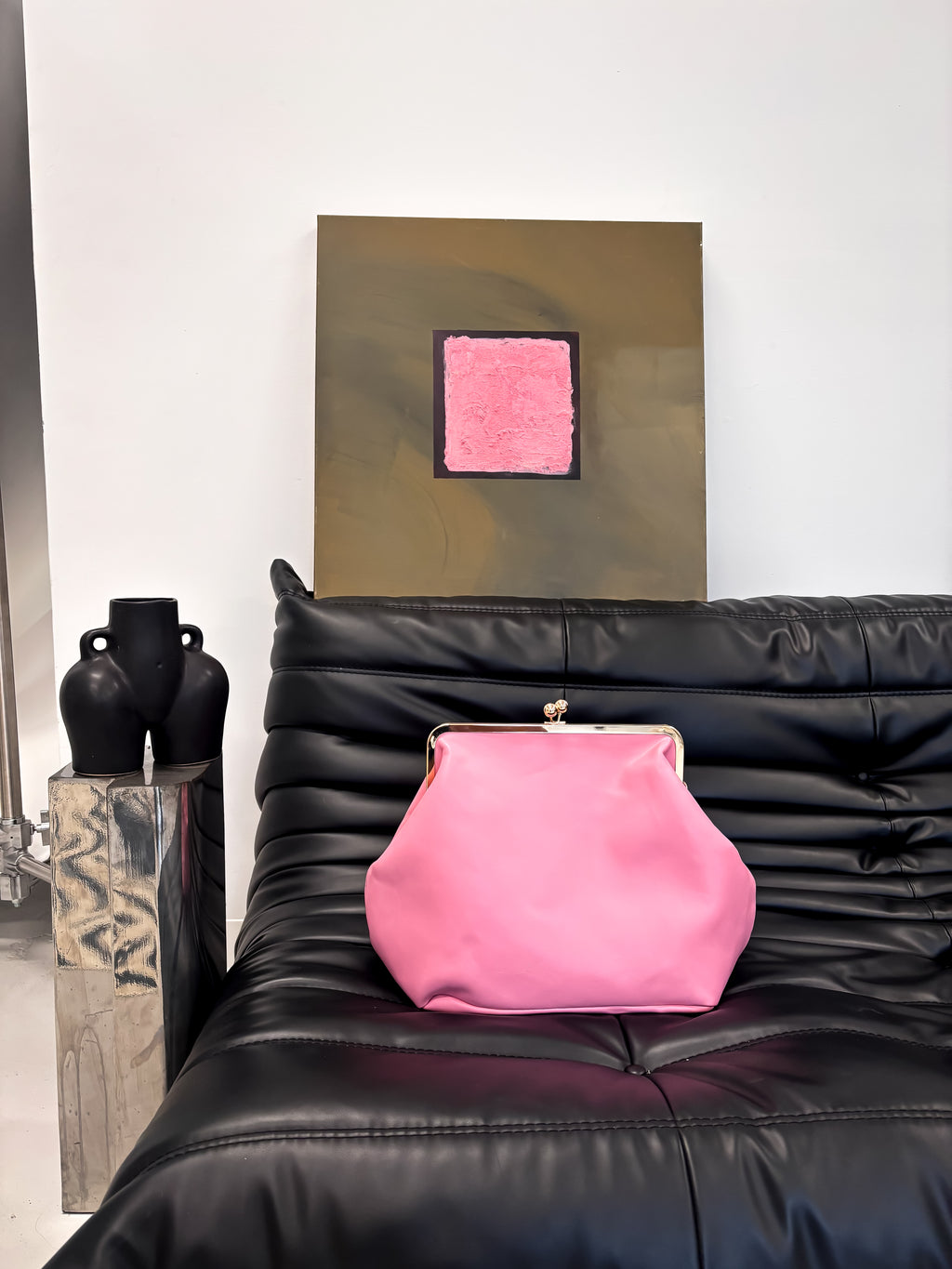 Pink clutch bag on a black leather sofa with abstract art in the background