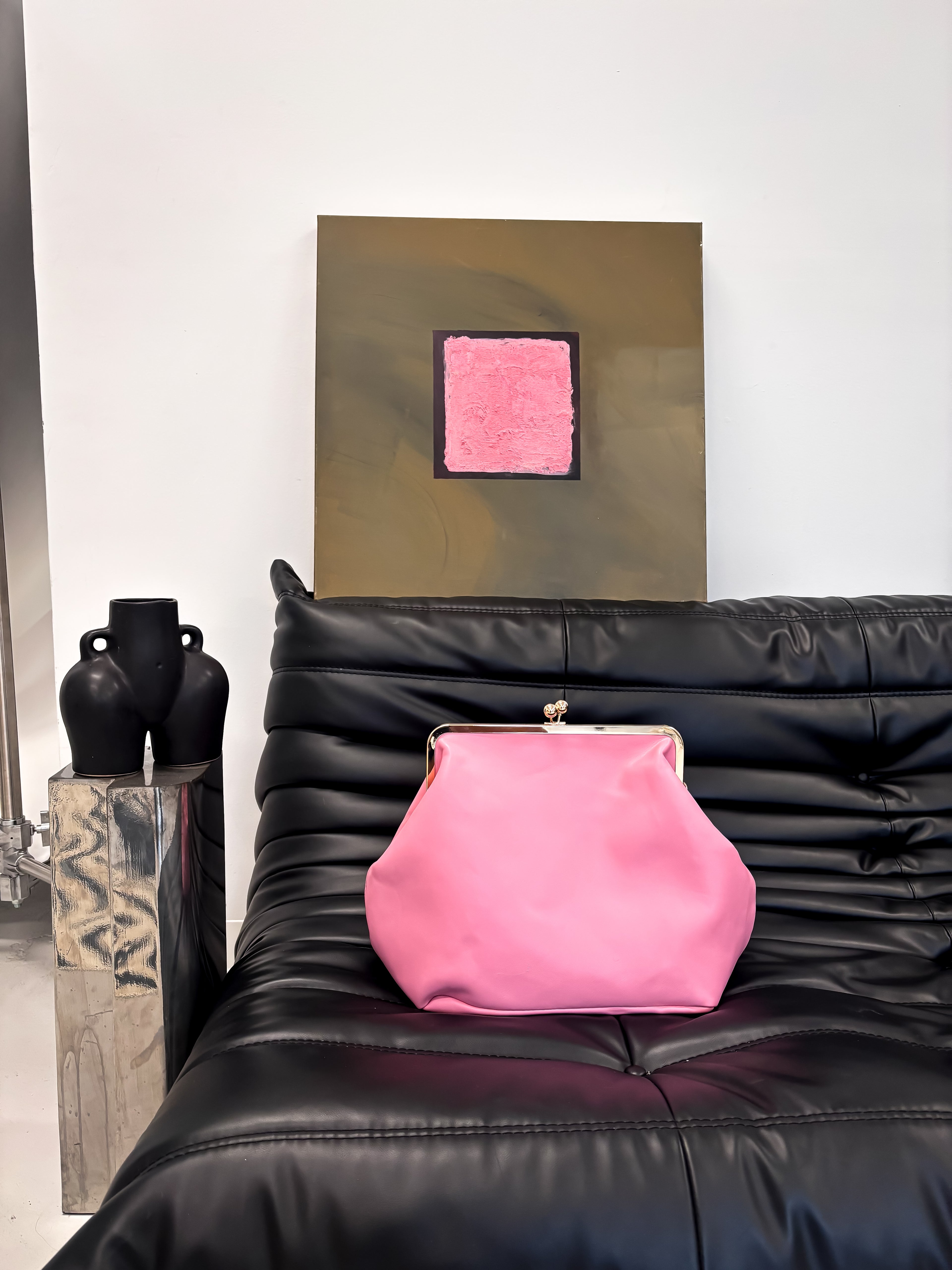 Pink clutch bag on a black leather sofa with abstract art in the background