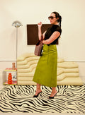 Woman in a greene midi skirt standing in a room with a zebra-patterned rug and modern furniture.